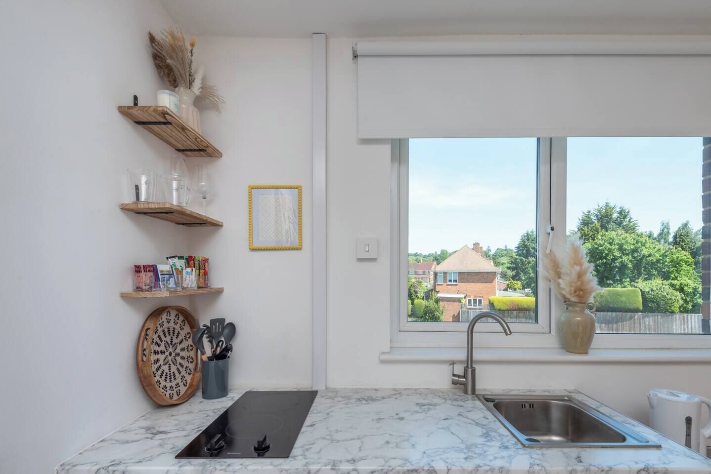 A modern kitchen with a marble countertop, a built-in stove, a sink, and a window with a view of houses.