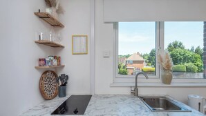 Een moderne keuken met een marmeren aanrecht, een ingebouwde kookplaat, een spoelbak en een raam met uitzicht op huizen.