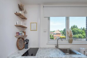 A modern kitchen with a marble countertop, a built-in stove, a sink, and a window with a view of houses. - #30 Cozy & Stylish Studio Retreat (Wooburn Green)