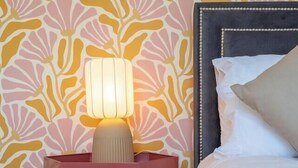 Een slaapkamer met behang met patroon, een bedlampje, een bed met kussens en een houten vloer.