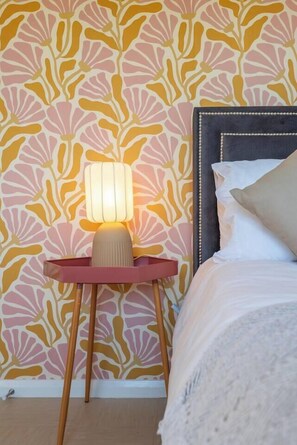 A bedroom with a patterned wallpaper, a bedside lamp, a bed with pillows, and a wooden floor. - #30 Cozy & Stylish Studio Retreat (Wooburn Green)
