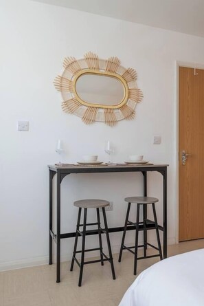A room with a bed, a table with two stools, a wall-mounted mirror, and a door. - #30 Cozy & Stylish Studio Retreat (Wooburn Green)
