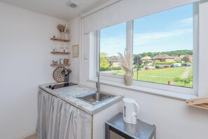 Una cocina con ventana, un lavamanos, una cafetera y vistas a una zona residencial.