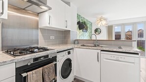 Ett modernt kök med gasspis, tvättmaskin och diskmaskin, med vita köksluckor och en bänkskiva i marmor.