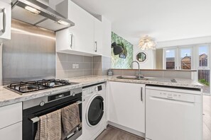 A modern kitchen with a gas stove, washing machine, and dishwasher, featuring white cabinetry and a marble countertop. - #28 Luxury 5bdr house|sleeps 11|near Bullring (West Midlands)