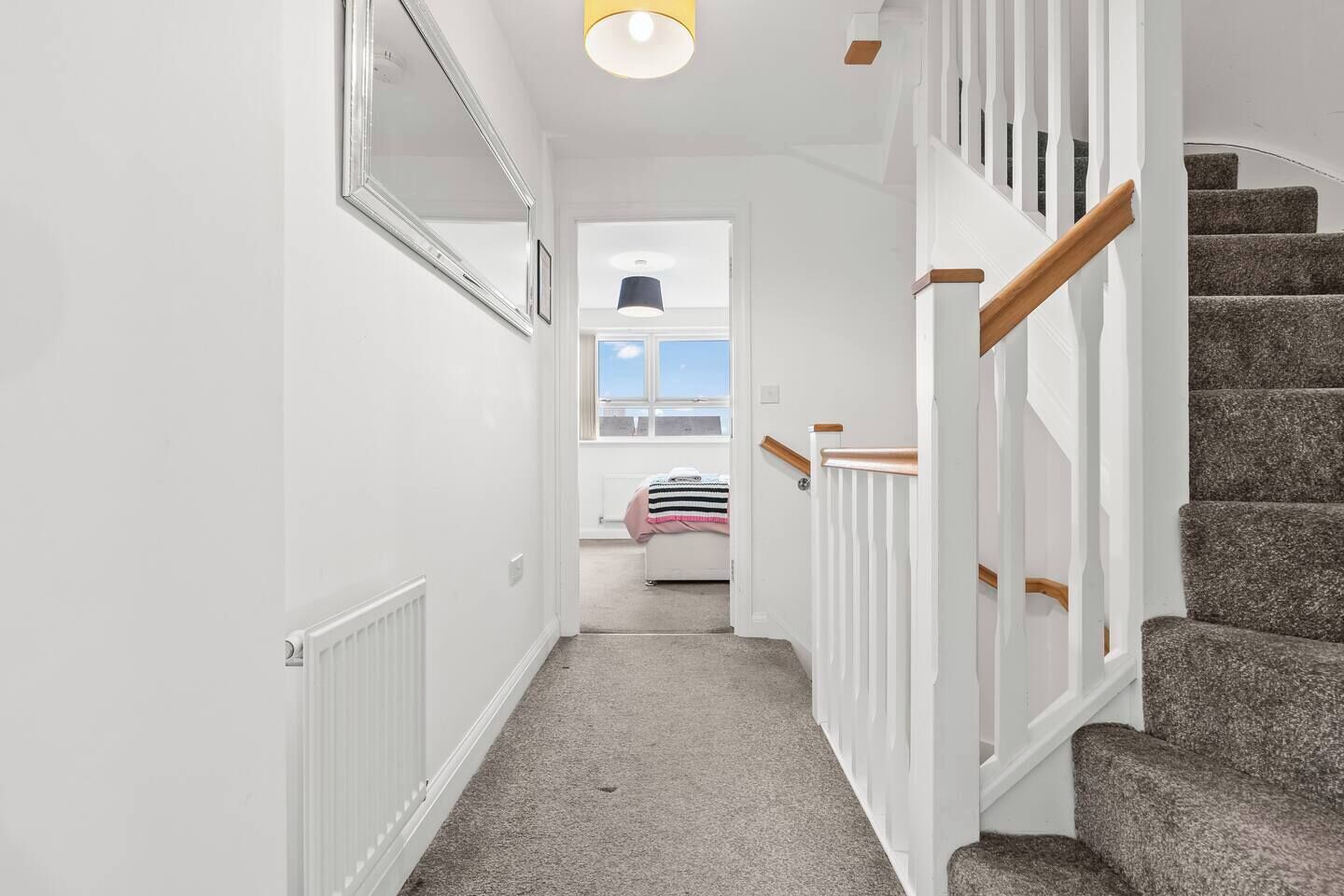 Ein Flur mit Treppe, weißen Wänden und einem Fenster zu einem Zimmer mit einem Bett.