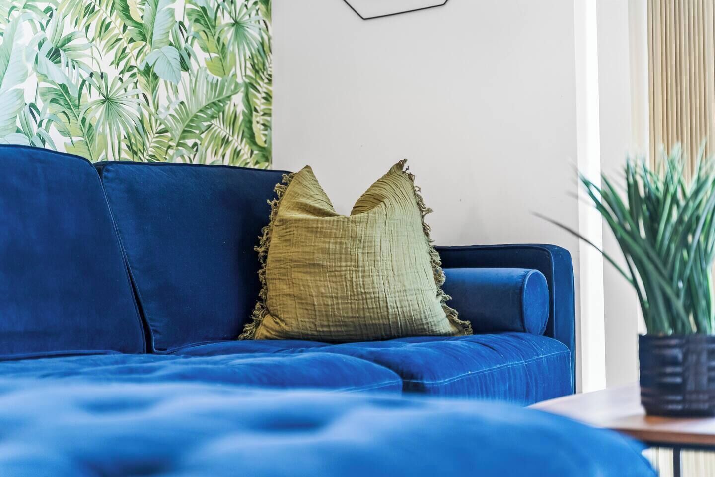 Ein blaues Sofa mit einem strukturierten Kissen, ein gerahmtes Bild an der Wand und ein Topfpflanzen auf einem Beistelltisch.