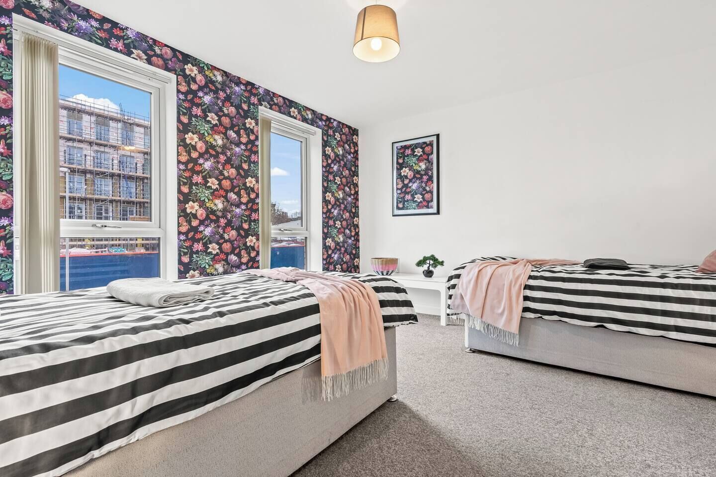 Una camera da letto con due letti, una finestra vista edifici e una parete con motivo floreale.