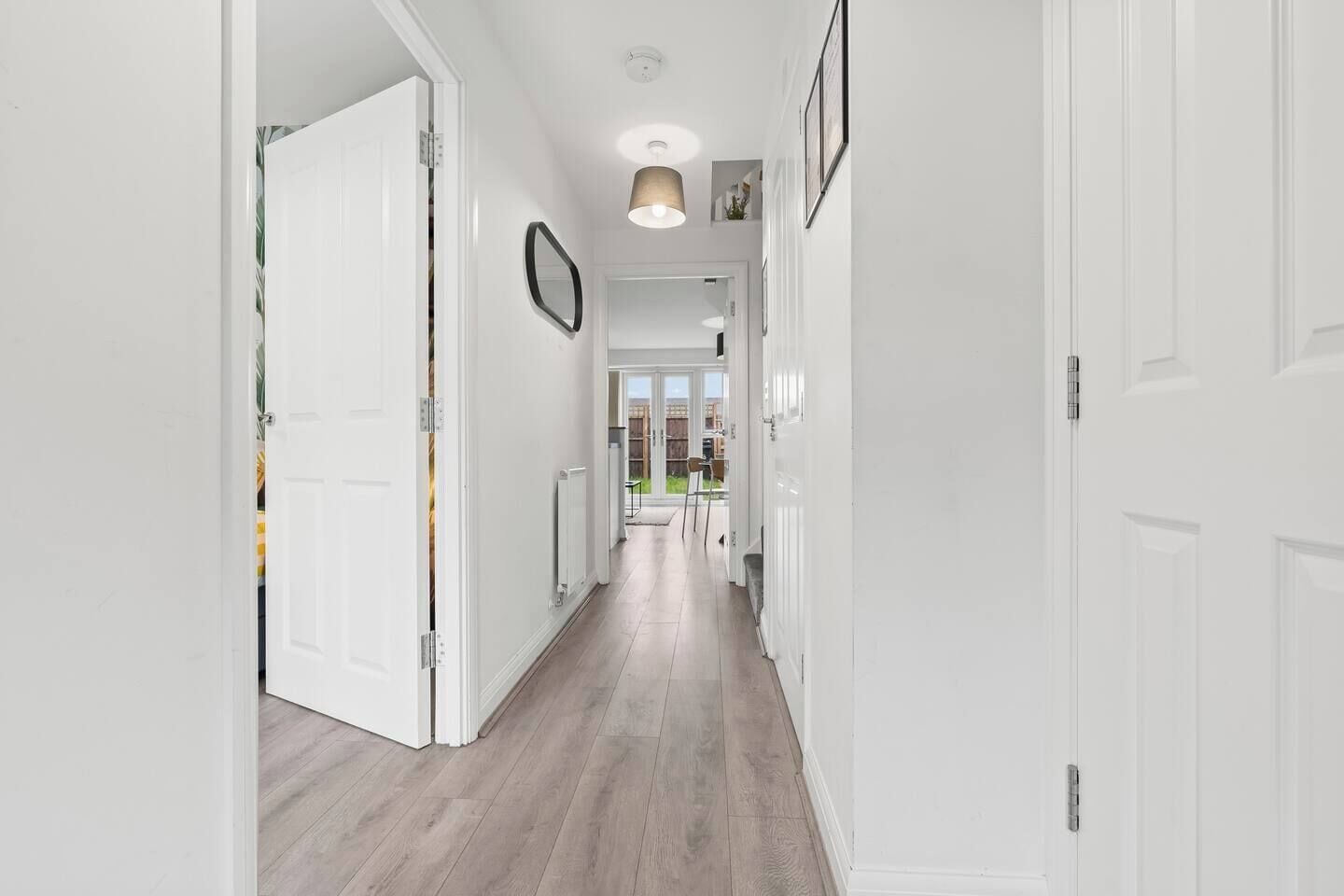 A hallway with white walls, a light wooden floor, and a ceiling light fixture.