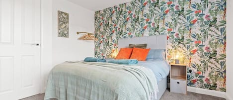 A bedroom with a bed, a nightstand, a wall-mounted lamp, and a door.