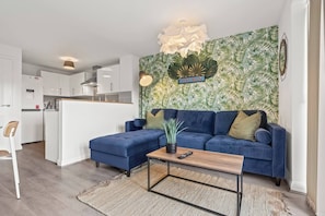 A modern living room with a blue sofa, a wooden coffee table, and a kitchen in the background. - #28 Luxury 5bdr house|sleeps 11|near Bullring (West Midlands)