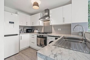 Una cocina moderna con armarios blancos, horno integrado, microondas, estufa y pileta de acero inoxidable.