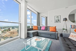 A modern living room with a large window, a glass coffee table, and a grey sofa with orange cushions. - #25 World Famous Rotunda 18th floor skyline views (West Midlands)