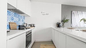 Moderni keittiö, jossa on valkoiset kaapit, sinisellä kuviolla koristeltu välitila ja ruostumattomasta teräksestä valmistettu liesituuletin.