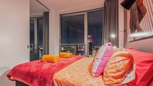 Hotellihuone, josta on näkymä kaupunkiin, kuviollinen vuodevaatteilla varustettu sänky ja suuri ikkuna.