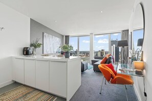 A modern kitchen with a large island, a dining area with orange chairs, and a view of the city through large windows. - #25 World Famous Rotunda 18th floor skyline views (West Midlands)