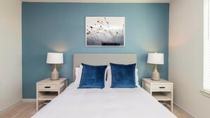 A bedroom with a bed, two bedside tables, two lamps, a headboard, and a wall-mounted picture.
