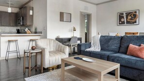 A modern living room with a sofa, armchair, coffee table, and a dining area with a kitchen in the background.