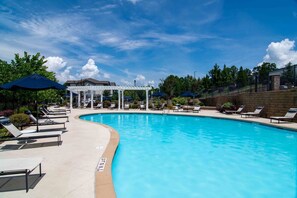 A swimming pool with lounge chairs and umbrellas, surrounded by a white pergola and a brick wall.