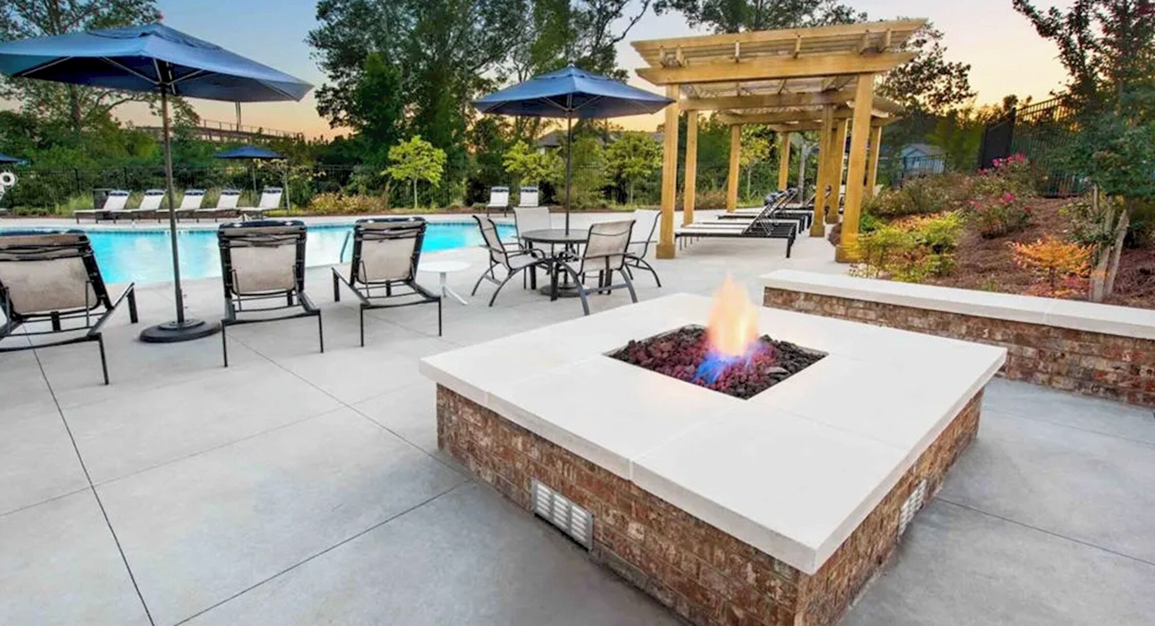 Un espacio al aire libre con un hoyo de fuego, sillones de descanso y una piscina.