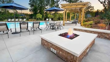 Un espacio al aire libre con un hoyo de fuego, sillones de descanso y una piscina.