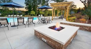 Un espacio al aire libre con un hoyo de fuego, sillones de descanso y una piscina.