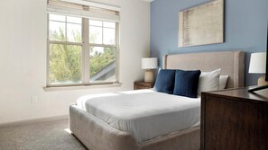 A bedroom with a large bed, a nightstand, a lamp, and a window with a view of trees. - Landing Amazing 1bd, Gym (Gainesville)
