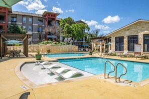A pool area with multiple swimming pools, lounge chairs, and a covered seating area. - Landing Chic 1bd, Pool, Gym (Austin)