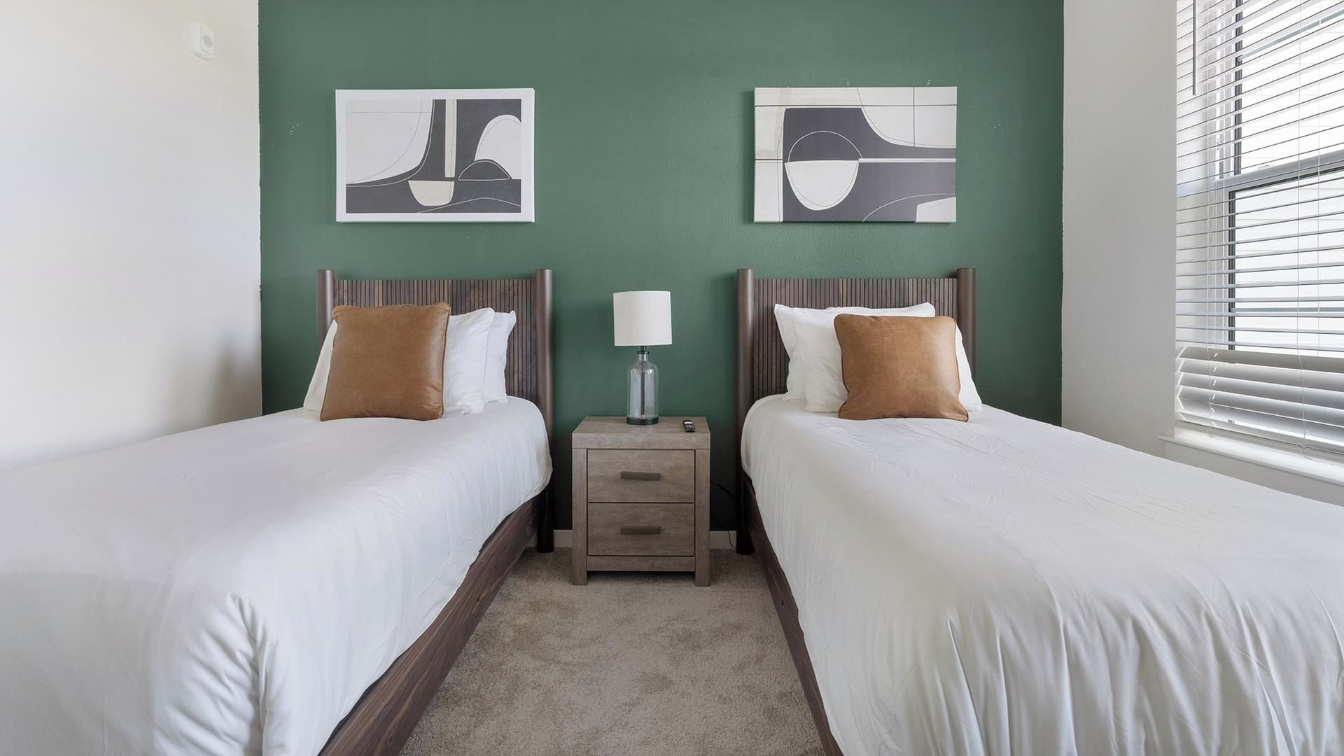 Een hotelkamer met twee bedden, een nachtkastje, een lamp en abstracte wanddecoratie.