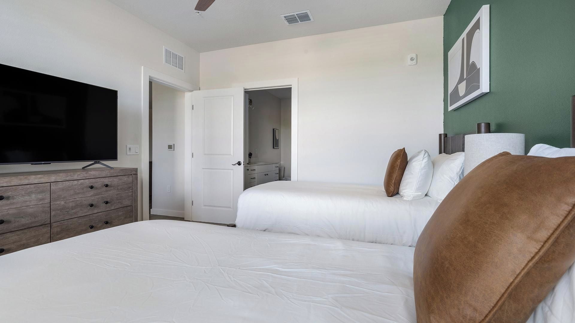 A hotel room with a bed, a dresser, a television, and a door leading to a bathroom.