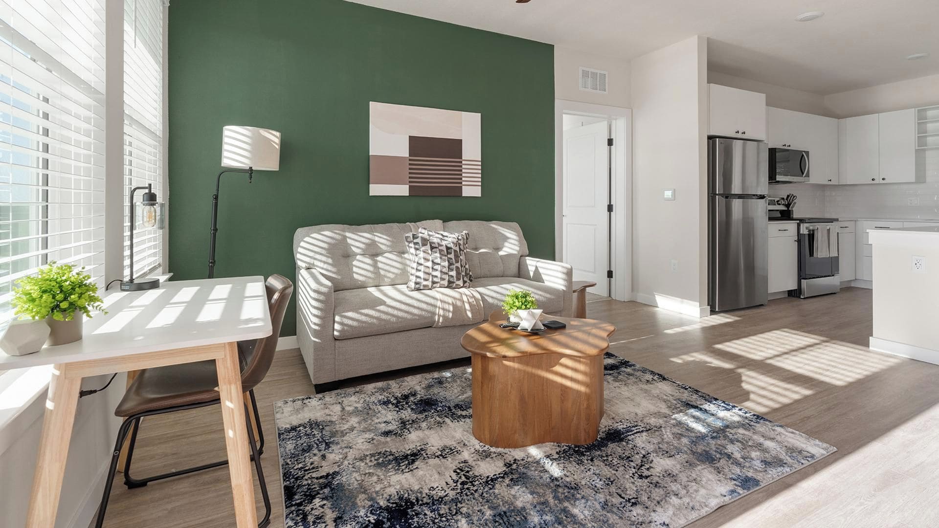 A modern living room with a green accent wall, a sofa, a coffee table, and a kitchen area with a refrigerator and microwave.