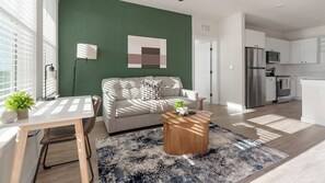 A modern living room with a green accent wall, a sofa, a coffee table, and a kitchen area with a refrigerator and microwave. - Landing Amazing 1bd, Yoga Studio, Game Room (Punta Gorda)