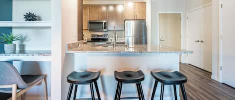 A modern kitchen with a central island, bar stools, and stainless steel appliances.