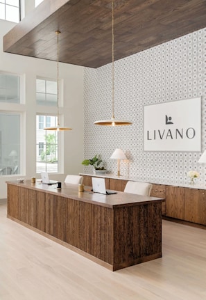 A modern reception desk with a wooden finish, two pendant lights, and a patterned wall with a 'LIVANO' sign. - Landing Beautiful 1bd, Gym, Clubhouse (Port Charlotte)