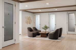 Ein geräumiger Raum mit modernem Design, ausgestattet mit einer Sitzecke, zwei Sesseln, einem kleinen Tisch, einer Topfpflanze und einer Tür mit der Aufschrift 'WORKPLACE'.