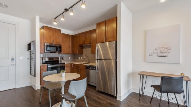 A modern kitchen with wooden cabinets, stainless steel appliances, a dining area with a round table and chairs, and a wall-mounted light fixture. - Landing Amazing 1bd, Pool (Katy)