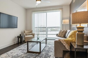 A modern living room with a sofa, armchair, glass coffee table, and a TV mounted on the wall. - Landing Amazing 1bd, Pool (Katy)