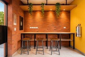 A kitchen area with a brick wall, wooden bar stools, a long table, hanging plants, and a fire extinguisher. - Contemporary Great View (Magdalena del Mar)