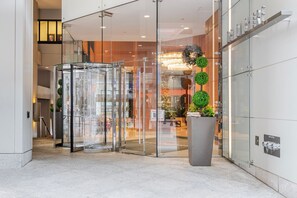 A modern hotel lobby with a revolving door, a large potted plant, and a glass wall displaying a Christmas tree. - Blueground | Financial District, pool, nr Boston Common (Boston)