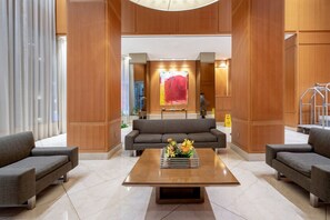 Um lobby moderno com área de estar central, uma grande pintura abstrata e painéis de madeira.