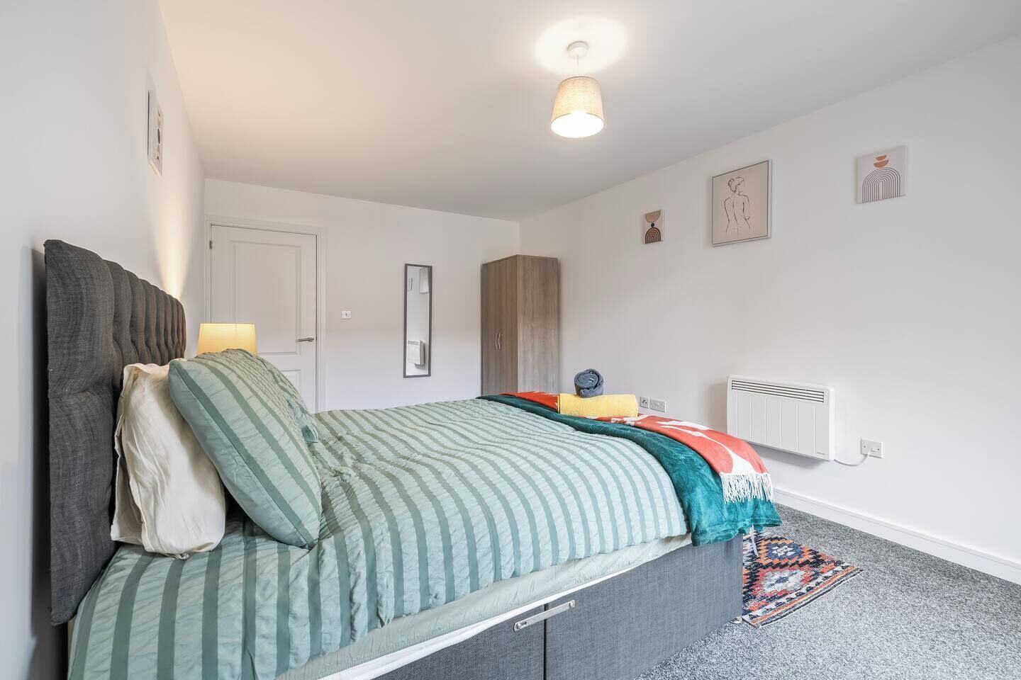 A bedroom with a bed, bedside lamps, a radiator, and wall art.