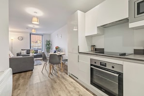 Eine moderne Küche mit weißen Schränken, einem eingebauten Backofen und einem Essbereich mit grauem Sofa und Esstisch.