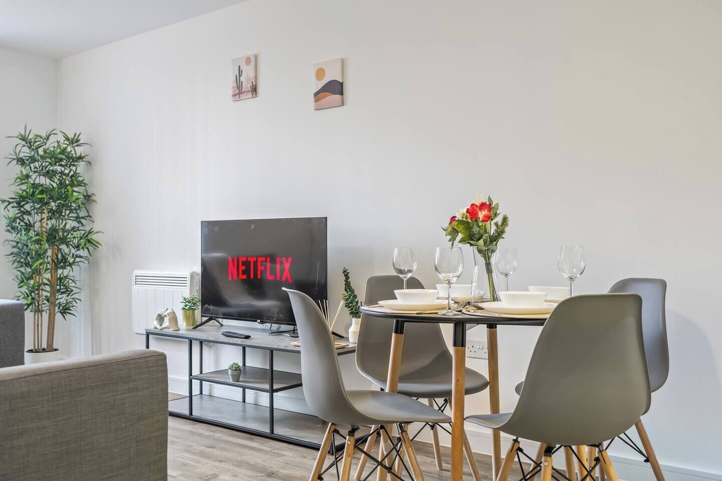 Een moderne woonkamer met een eetgedeelte, een flatscreen televisie waarop 'NETFLIX' wordt weergegeven, en een kamerplant.