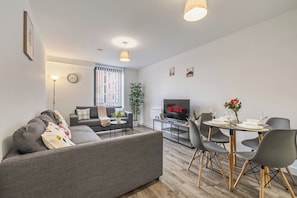 A modern living room with a grey sofa, a dining table with chairs, a flat-screen TV, and a potted plant. - #70 City Hideaway|sleeps 4|near The CustardFactory (Deritend)