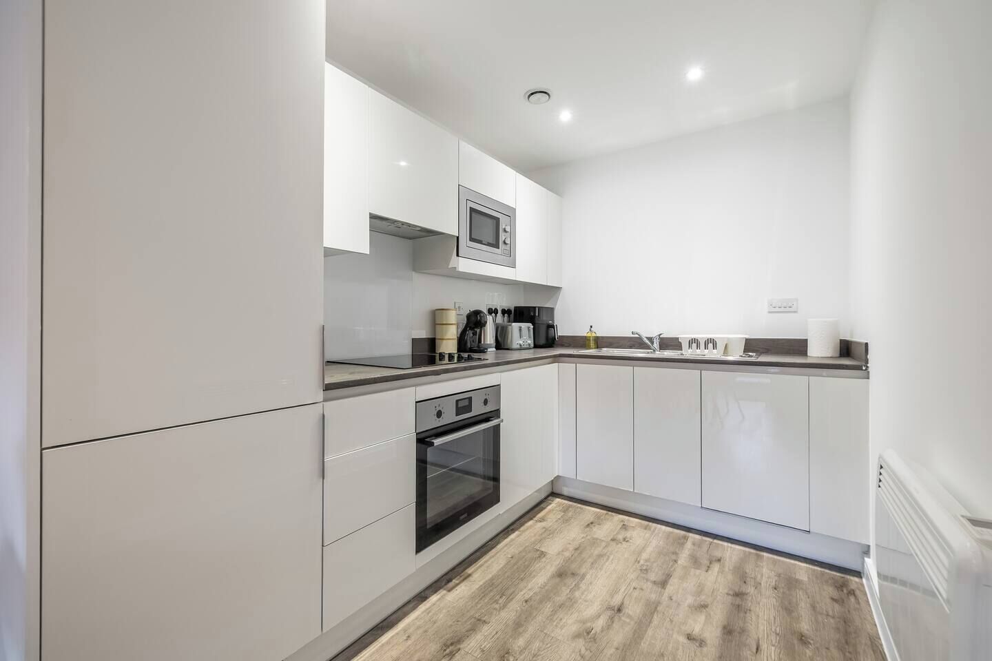 A modern kitchen with white cabinetry, a built-in oven, a microwave, and a wooden floor.