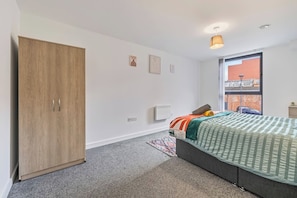 Ein Schlafzimmer mit Bett, Kleiderschrank, Heizkörper und Fenster mit Blick nach draußen.