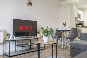 A modern living room with a flat-screen TV displaying 'NETFLIX,' a dining area with a table and chairs, and a kitchen in the background. - #70 City Hideaway|sleeps 4|near The CustardFactory (Deritend)