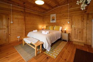 A wooden room with a bed, bedside tables, a bench, and a rug. - #67 Private Hot Tub Reindeer Lodge retreat (Blithbury)