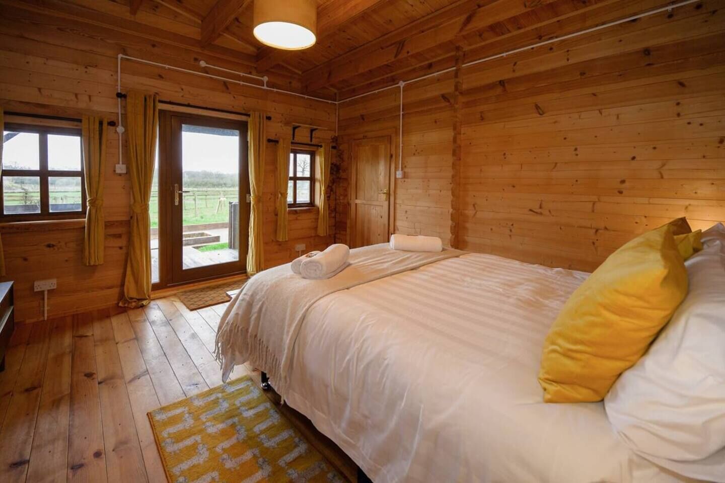 A wooden cabin bedroom with a bed, curtains, and a view through the door.