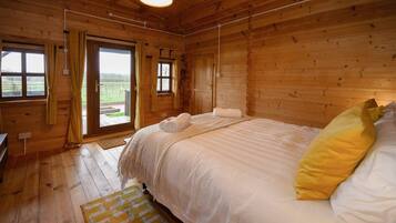 A wooden cabin bedroom with a bed, curtains, and a view through the door.